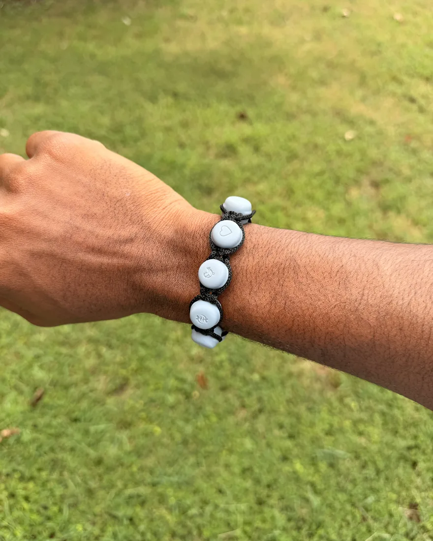The first bracelet built on the flex spine, worn outdoors: pale grey beads engraved with Adinkra symbols on a black braided cord